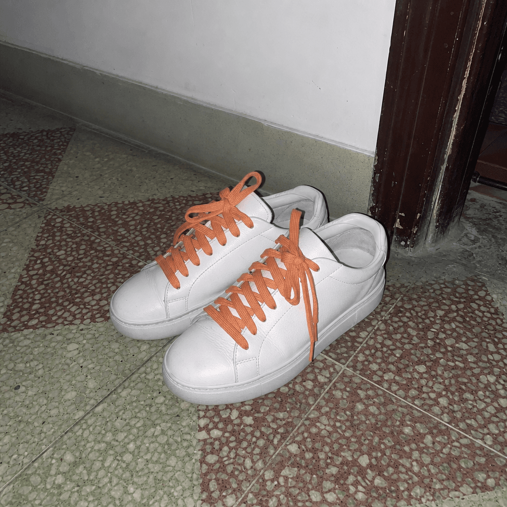 Paire de baskets blanches à lacets orange posée sur un sol carrelé
